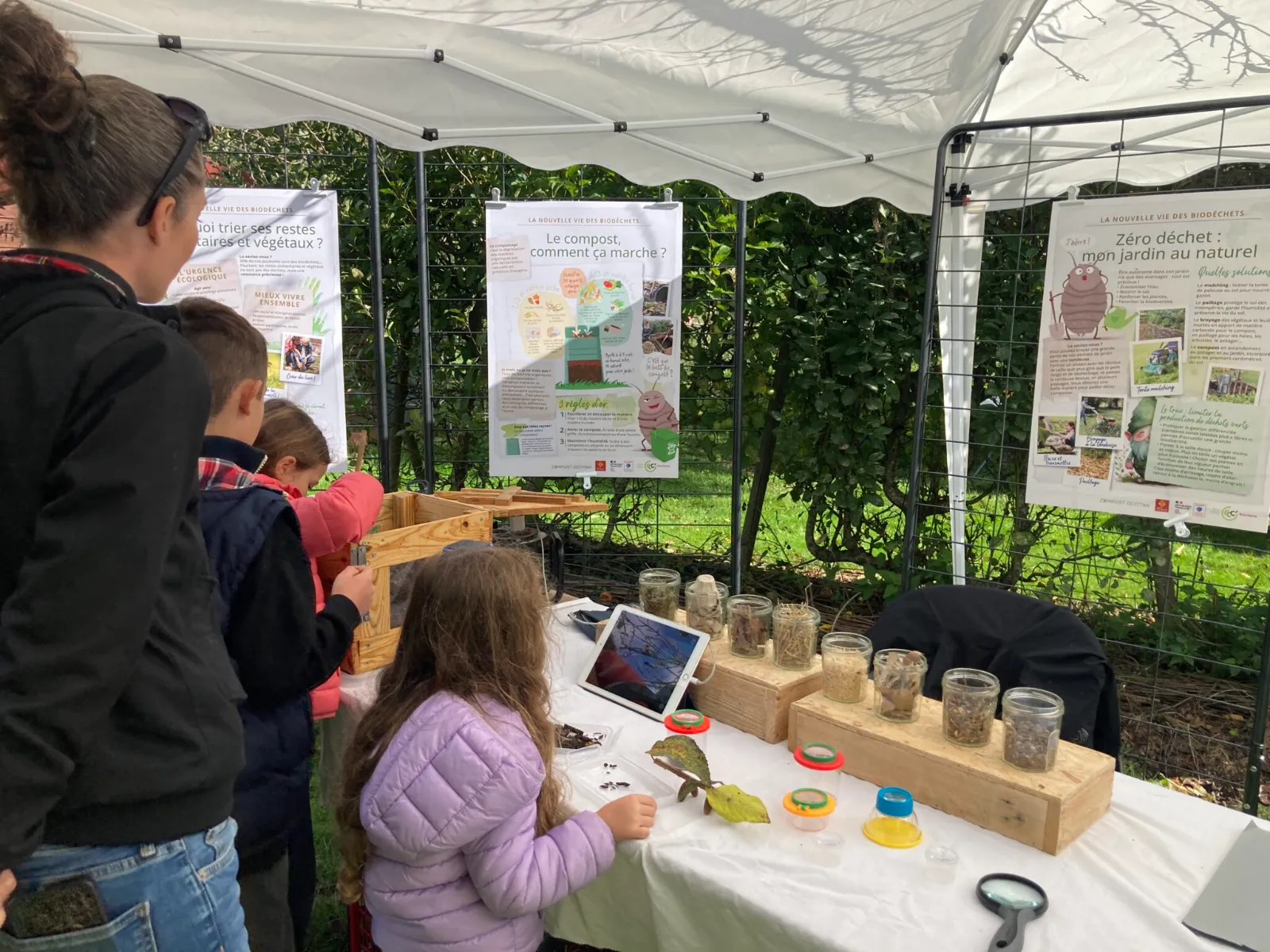 Stand de sensibilisation au compostage : enfants découvrant des bocaux de matières compostables et des panneaux pédagogiques